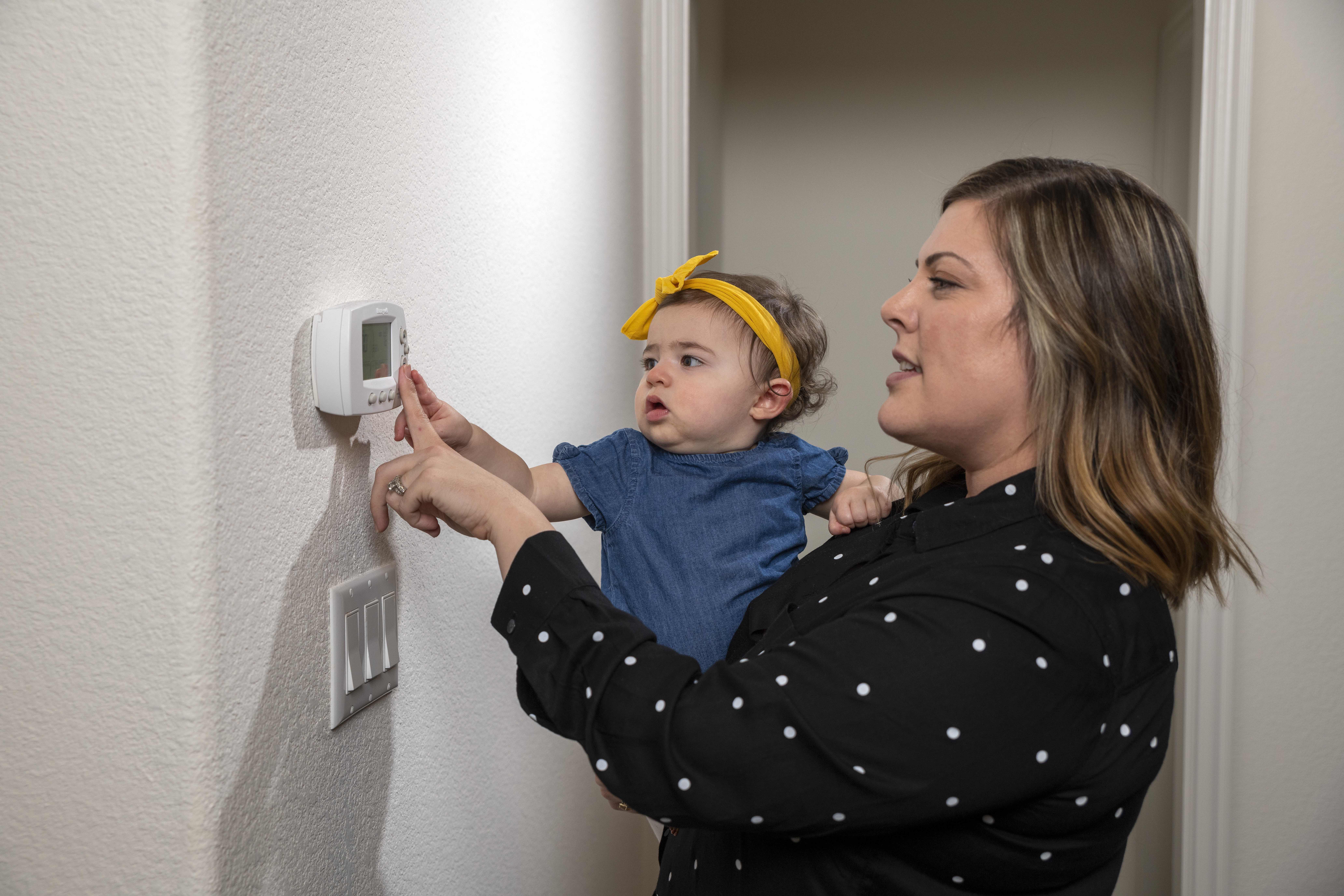 Energy Saving Tips Mom holding a baby and adjusting the thermostat